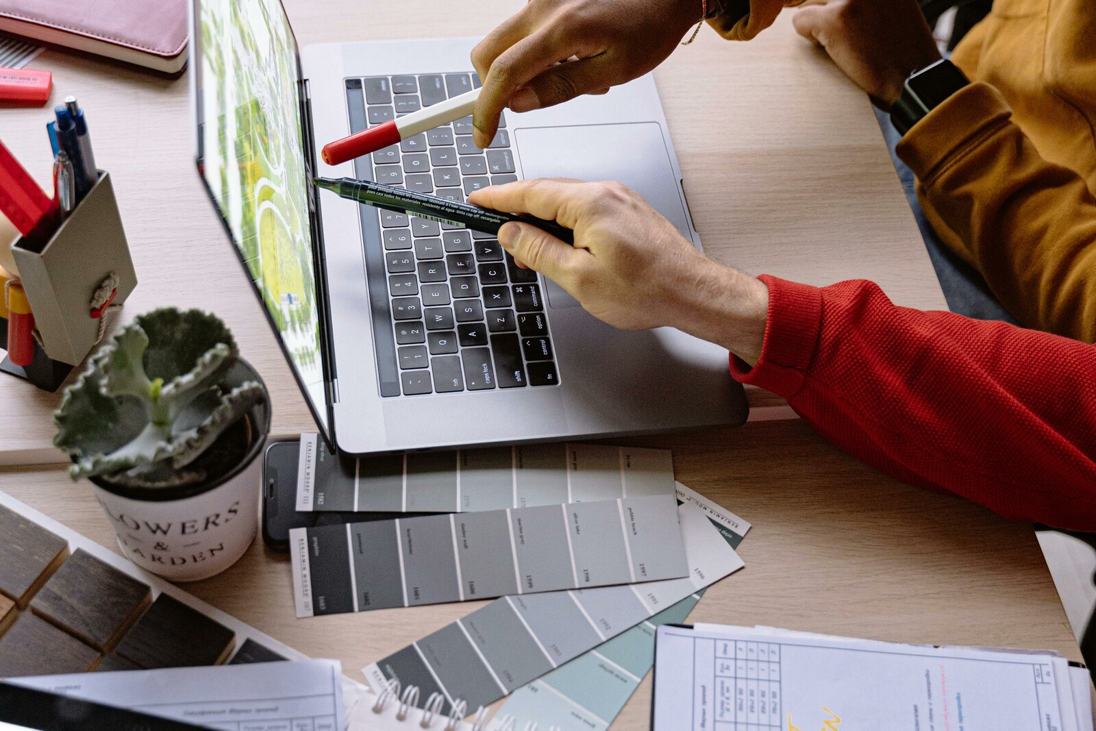 Два человека указывают на экран ноутбука с рабочими материалами на столе