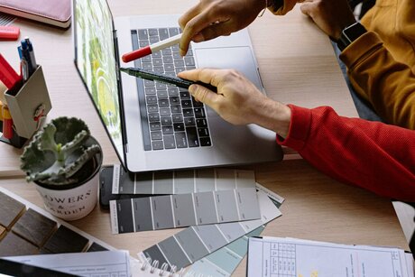 Два человека указывают на экран ноутбука с рабочими материалами на столе